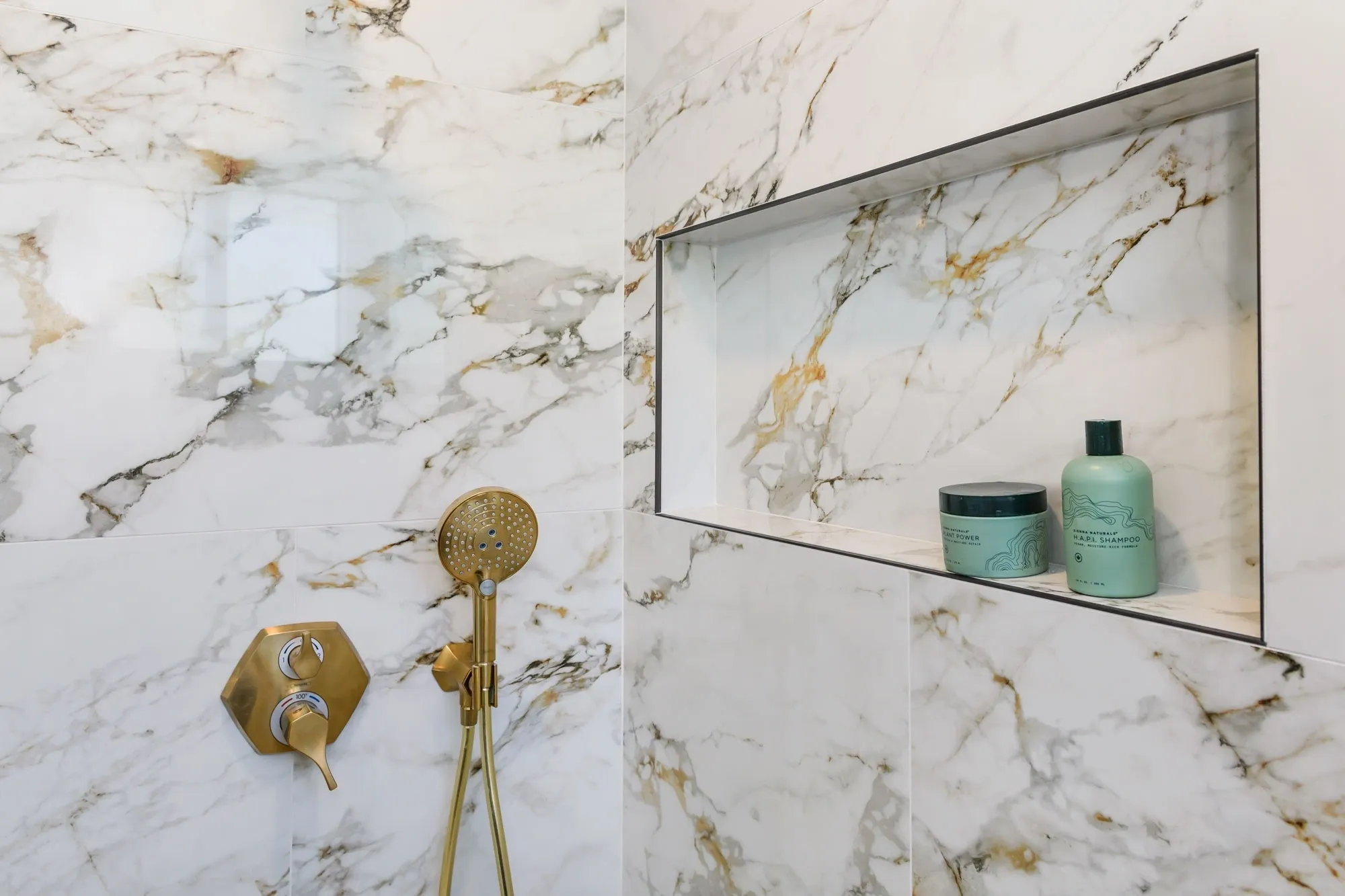 Marble shower with gold fixtures and niche